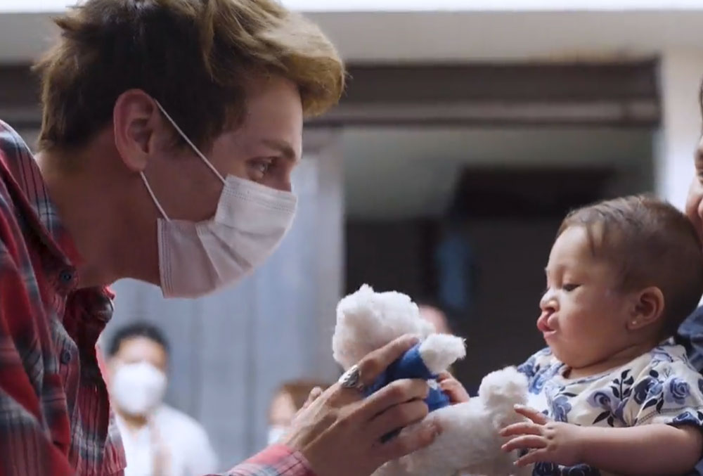 Jacob Bertrand handing a Smile Train teddy to a patient at her house