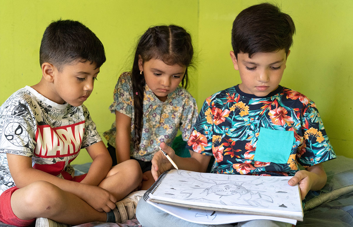 Joaquin drawing while his sister and another child look on