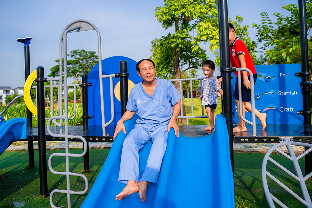 Dr Hoc Trinh going down a slide at a playground with his patients Dat and Quy