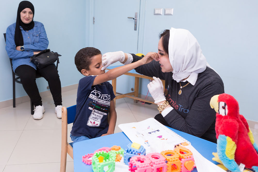 Dr Sally working with a Smile Train speech patient, holding his nose