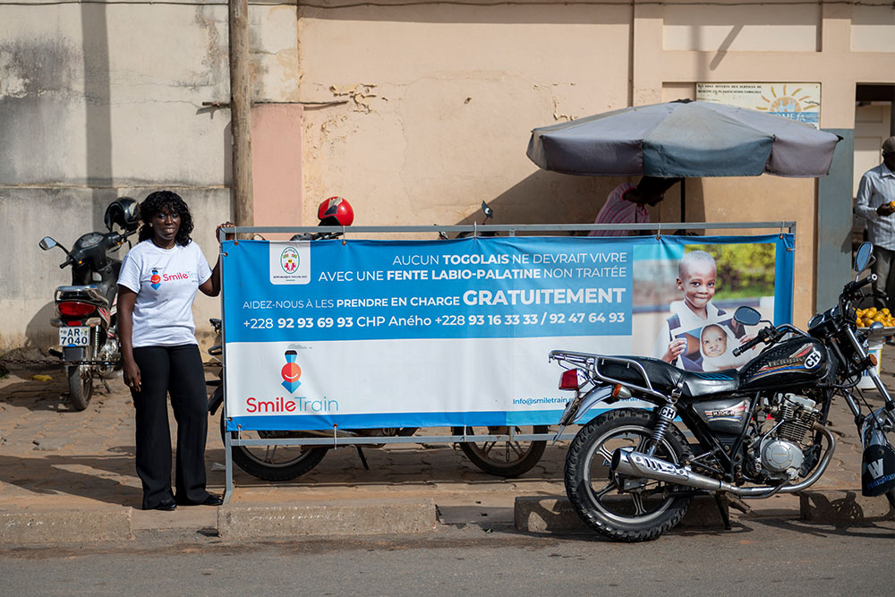 Nina standing next to a roadside banner for Smile Train’s services in Togo