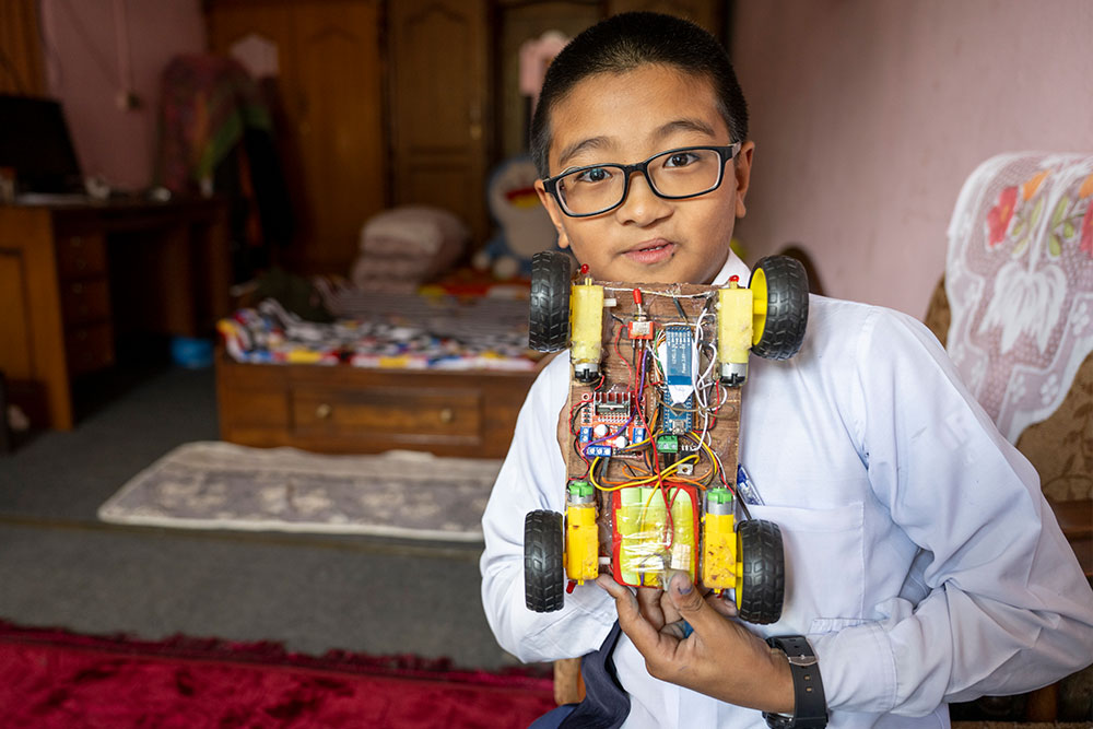 Jenious holding up a robot car he made with his dad