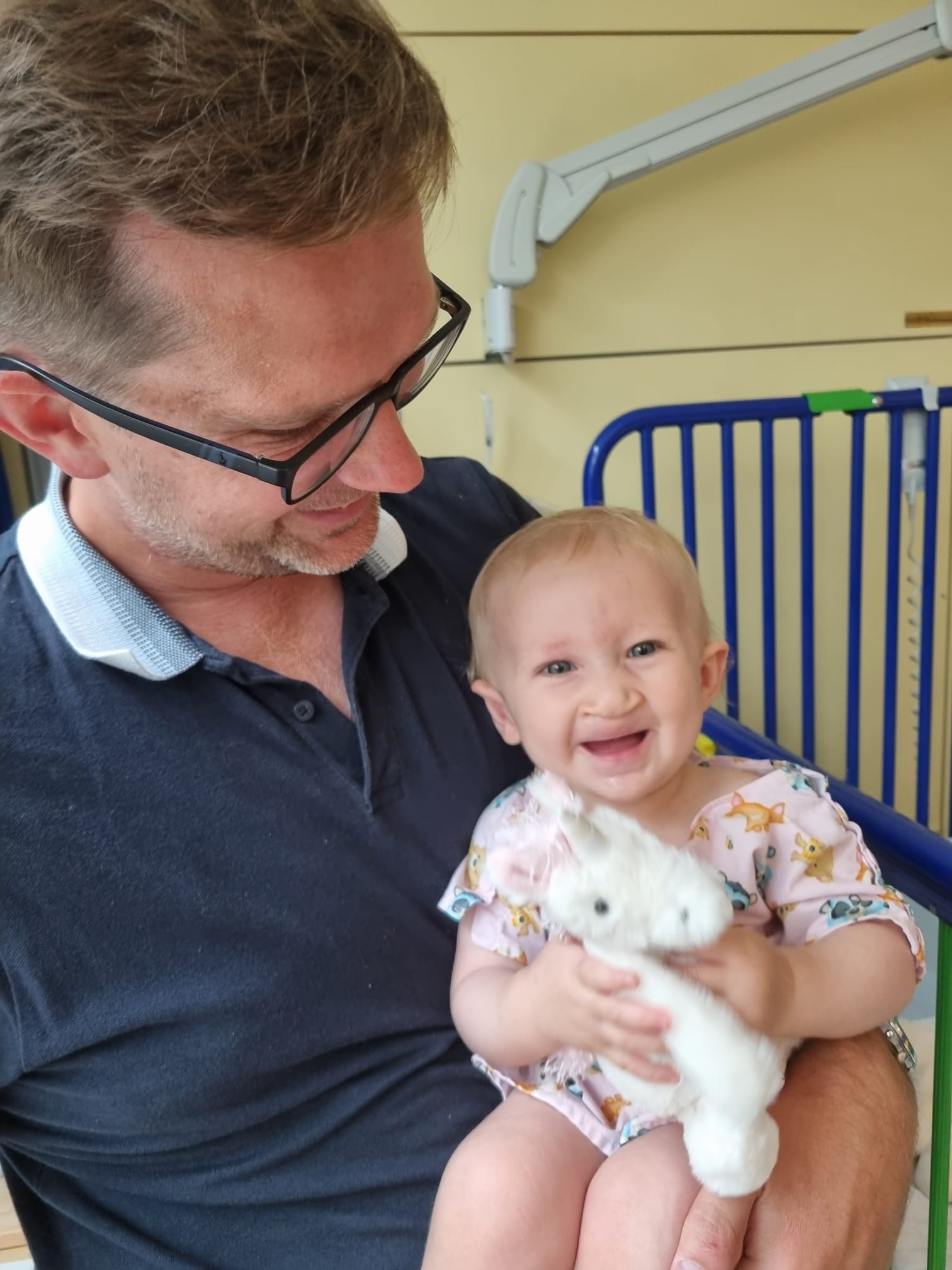 Patrick holding baby Anya. She’s in a hospital gown and holding a stuffed unicorn