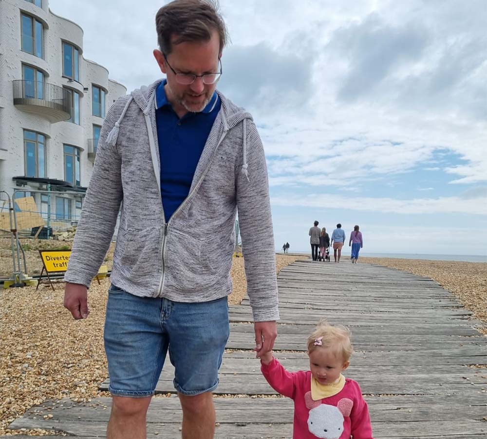 Patrick and baby Anya walking hand in hand on a boardwalk