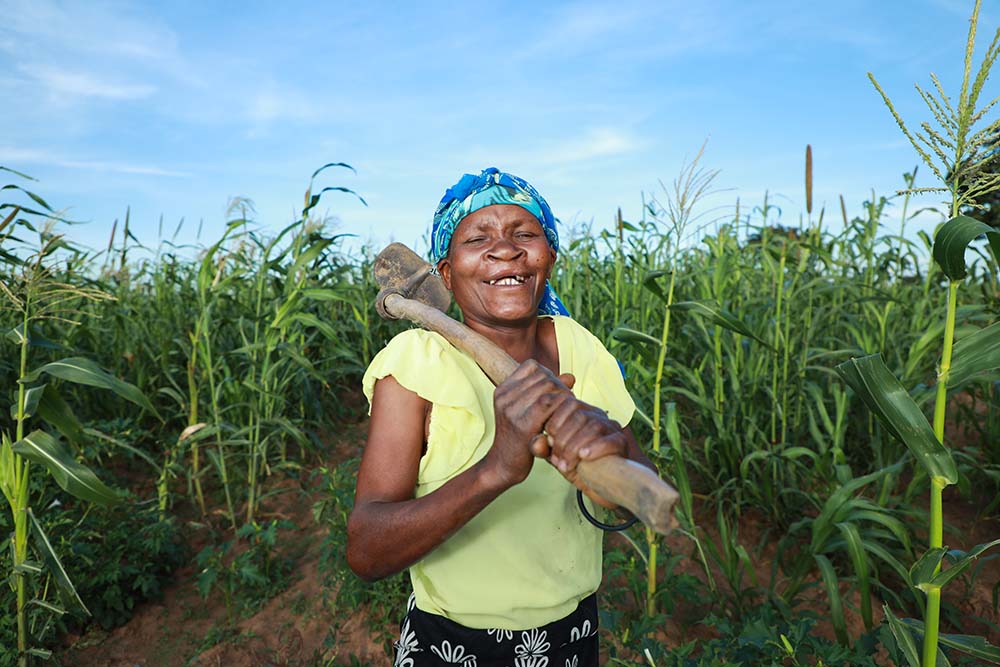Zita smiling and holding a hoe in front of her crops