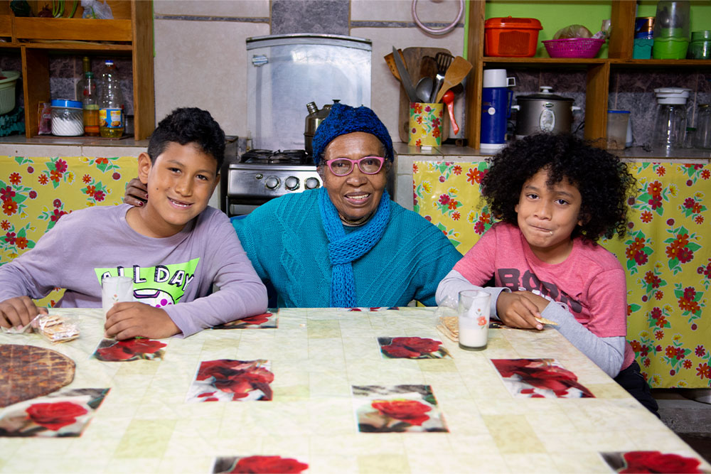 Imanol, his great aunt, and his little brother sitting at the kitchen table together with glasses of milk
