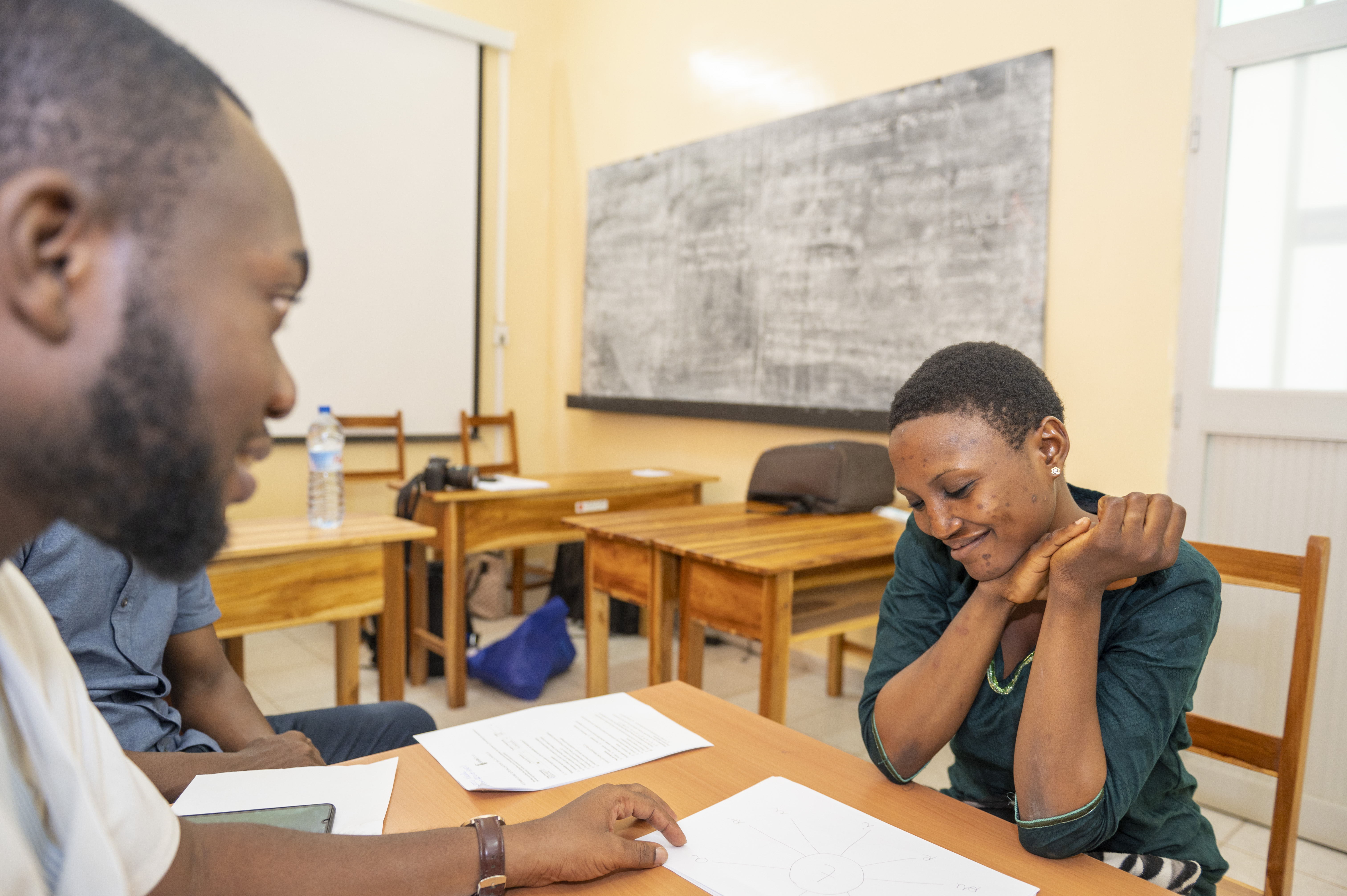 A woman sitting across from Faysal at speech therapy, smiling down at some papers