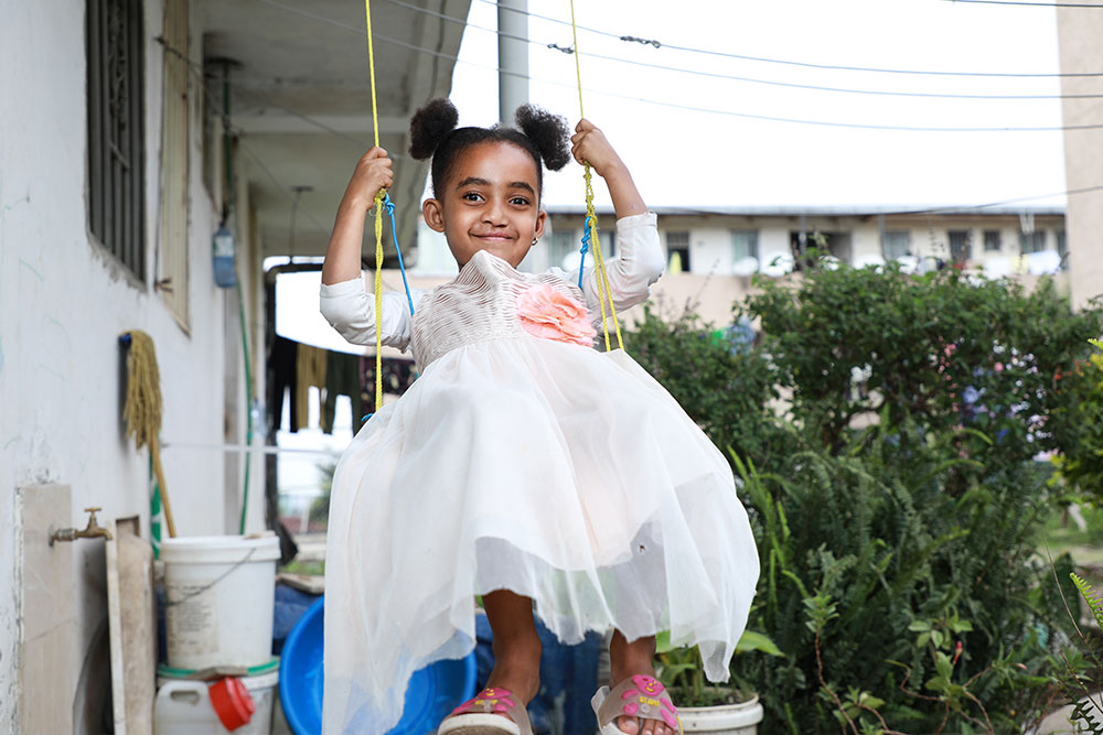 Marsillas smiling, in a white dress standing on a swing