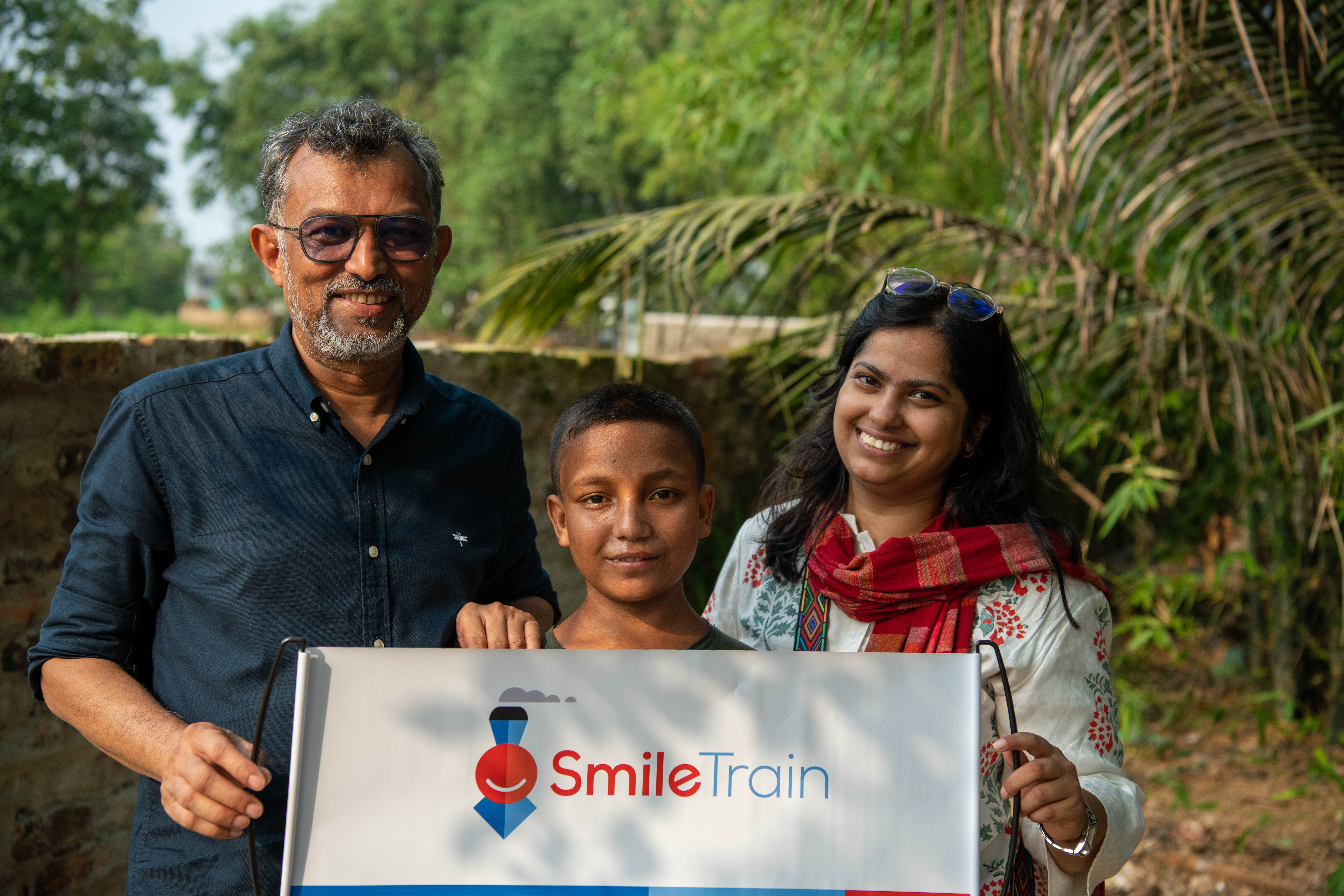 Mobasher with Shamima Nawsin, Smile Train’s Program Manager for Bangladesh and a patient. They are all holding a Smile Train banner