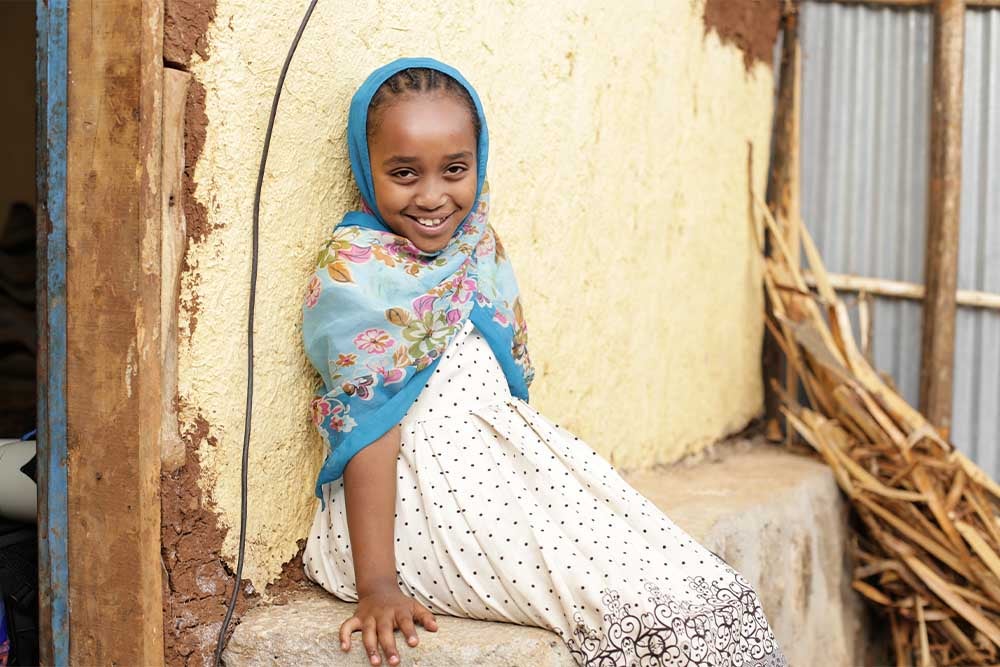 Mariam sitting on a ledge and smiling at the camera