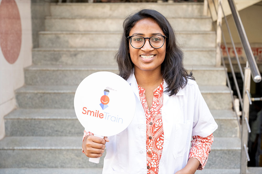 Dr. Mayuri Kalyanpad smiling in a lab coat holding a Smile Train sign