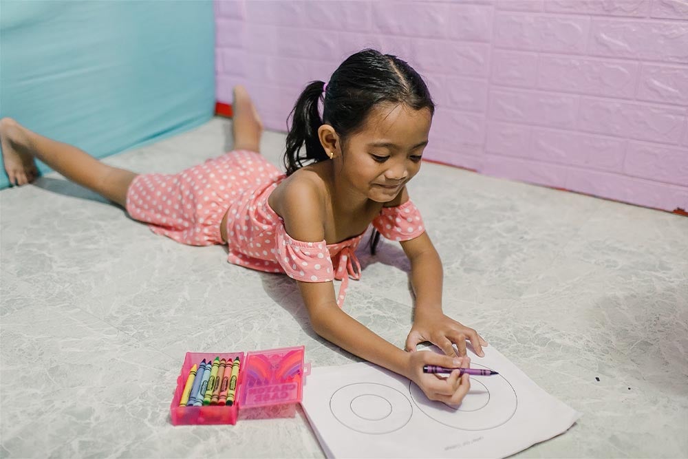 Leana laying on the floor colouring a colouring sheet with crayons