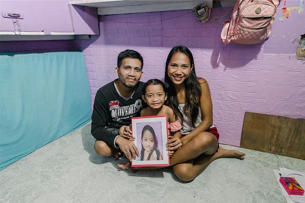 Leonardo, Leana, and Ranelyn sitting on the floor holding a photo of Leana before cleft surgery