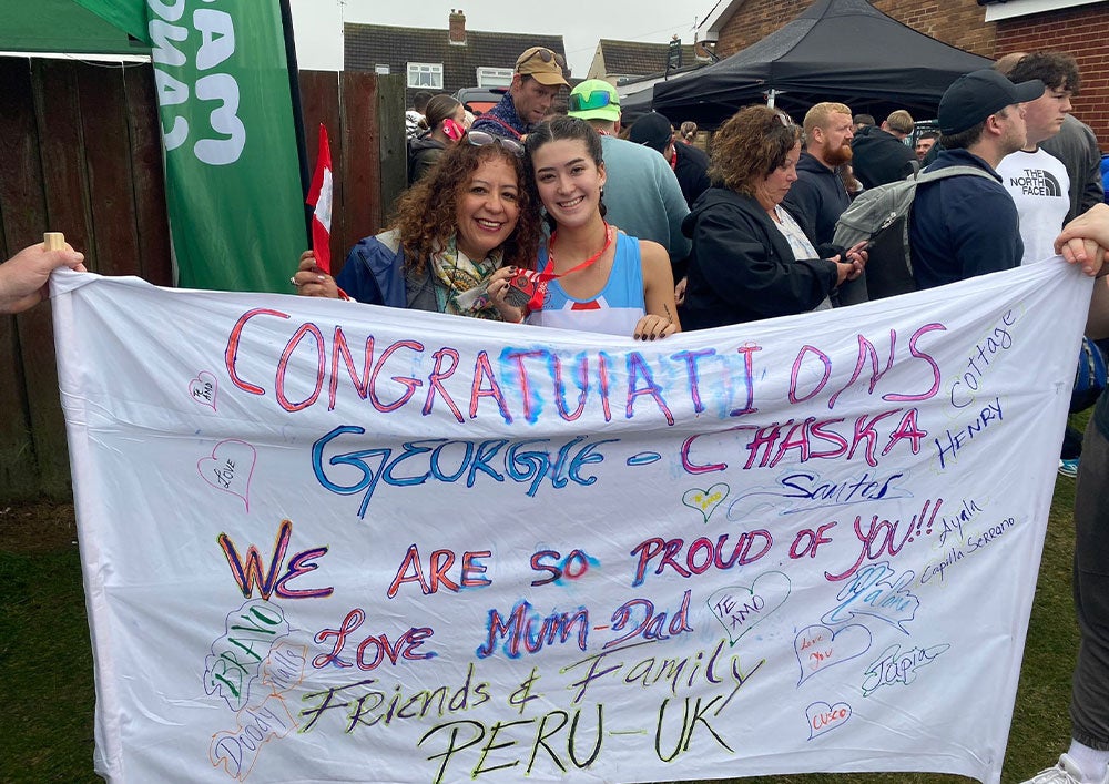 Georgina standing with her mum behind a sign large sign filled with well-wishes from family and friends during the race. She is wearing her medal around her neck