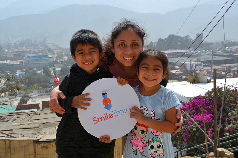 Astrid smiling with Lissette and her brother and holding a Smile Train sign after cleft surgery