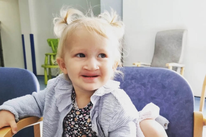 Anya sitting in a waiting room chair after cleft surgery, holding a doll