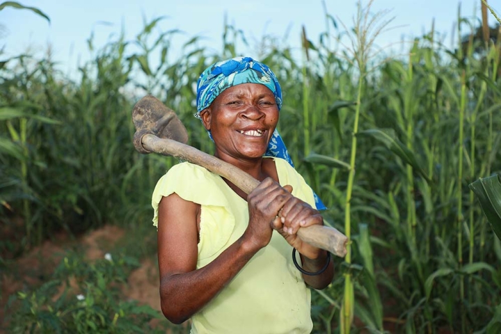 Zita smiling and holding a hoe in front of her crops