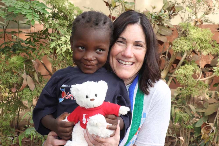 Fatima Kamara smiling and holding a Smile Train teddy bear with Susannah Schaefer after cleft surgery