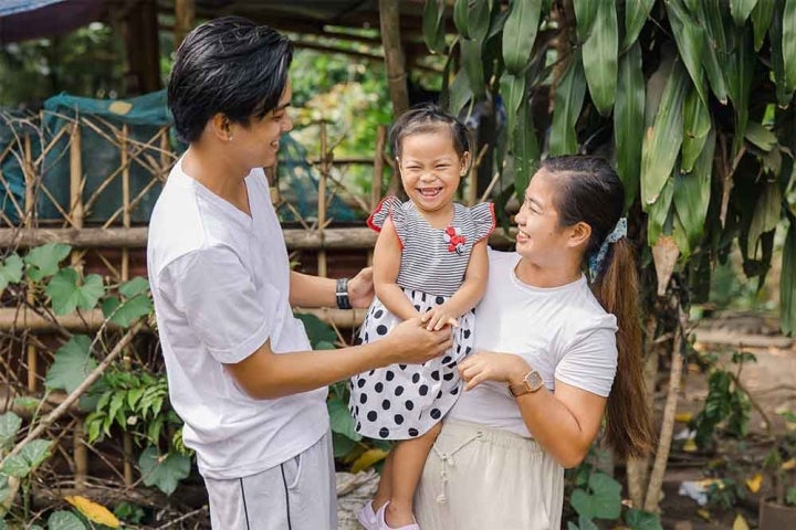 Selma, Ken, and their daughter, Kaylee, all share wide, affectionate grins. Selma holds Kaylee in her arm